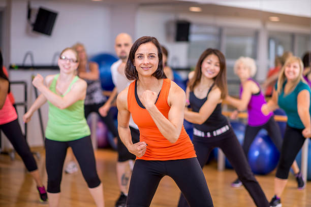 A multi-ethnic group of adults are taking a dance fitness class together at the the gym.